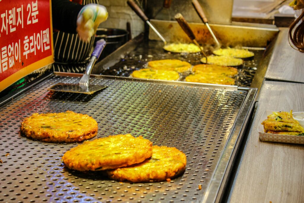 Korean street food pancakes (Hotteok or Pajeon) being fried on a hot griddle