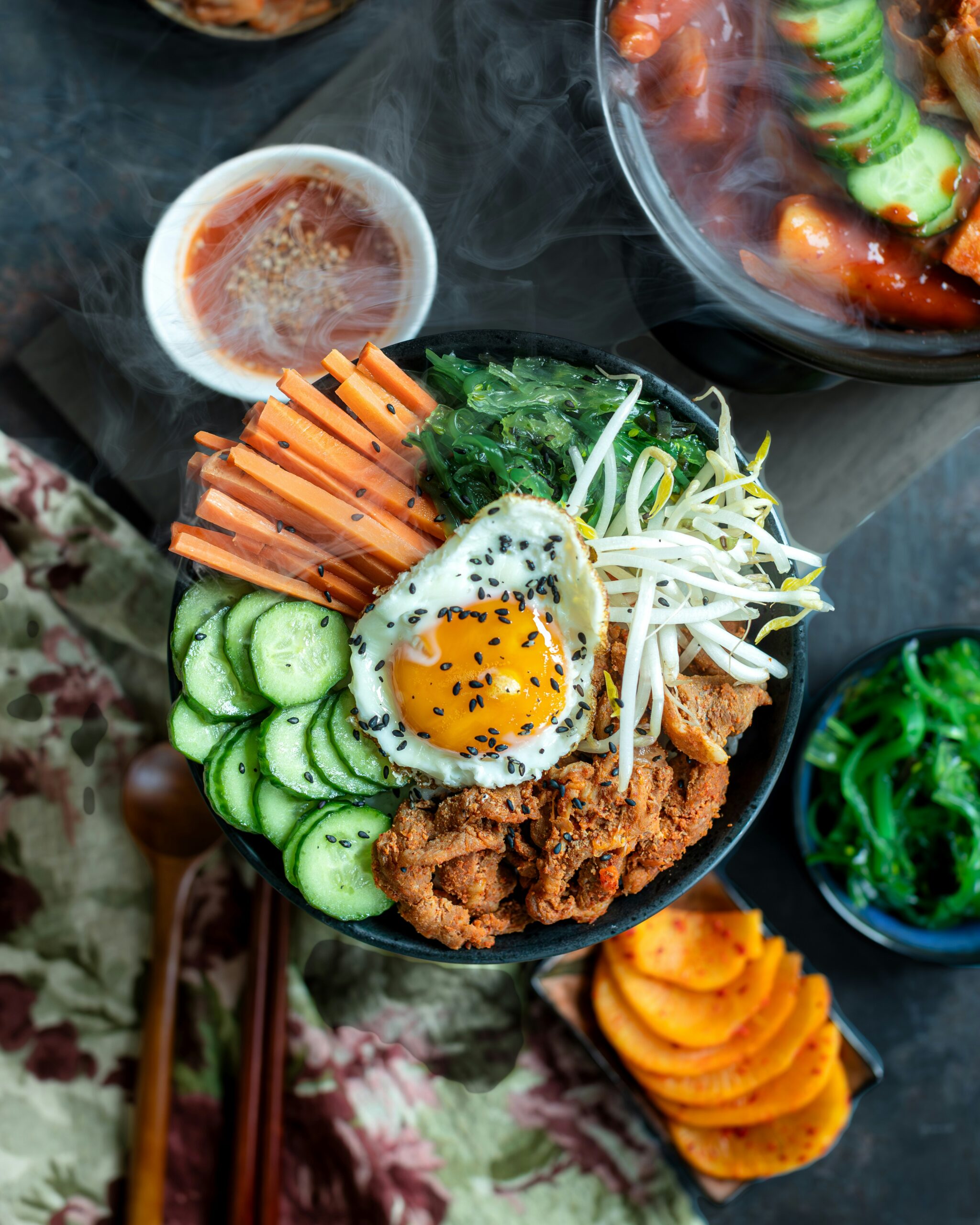 A beautifully arranged bibimbap bowl with spicy marinated meat, fresh cucumber slices, julienned carrots, seaweed salad, bean sprout