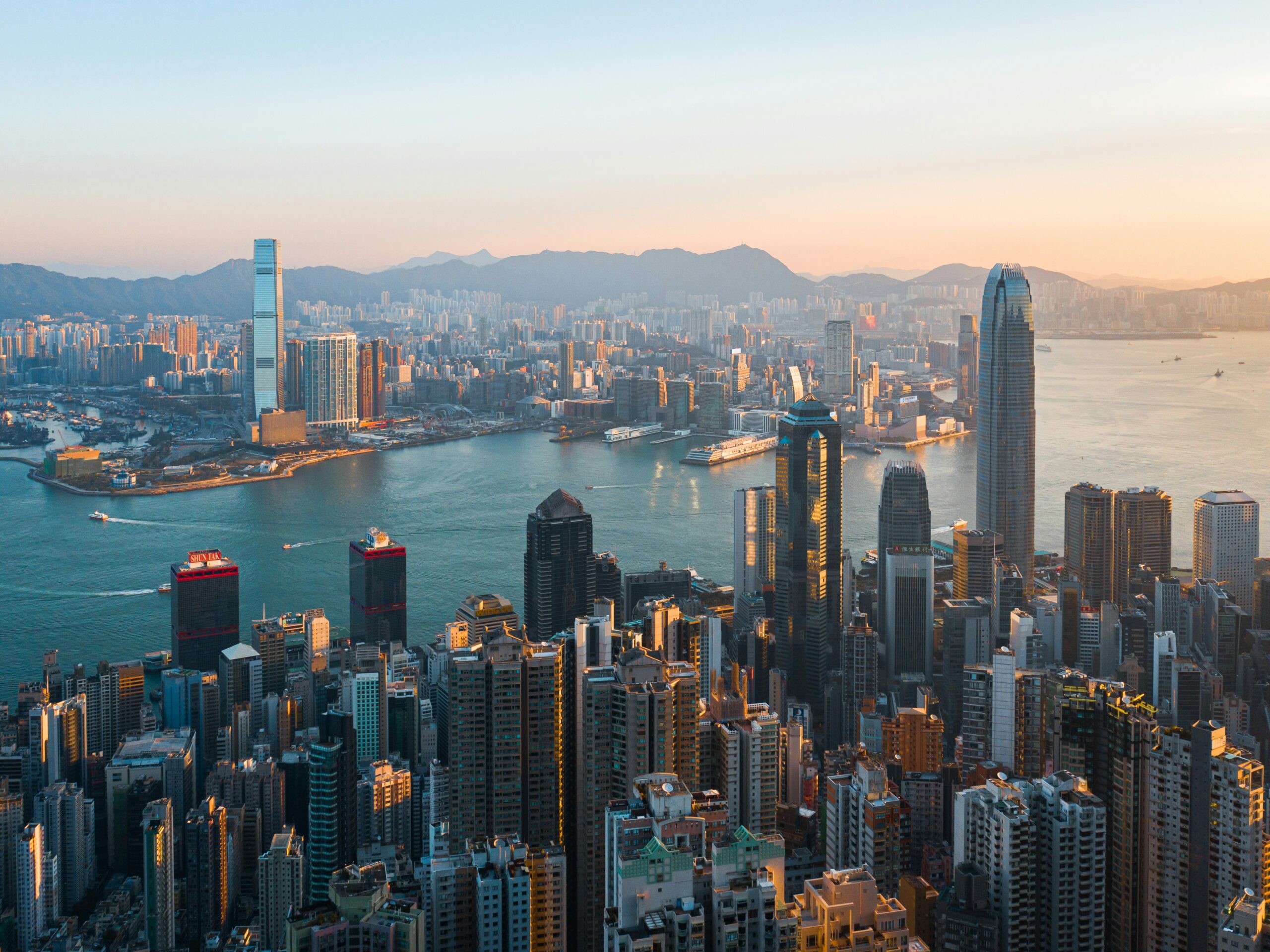 A breathtaking aerial view of Hong Kong's skyline at sunset, showcasing a dense cluster of skyscrapers along Victoria Harbour