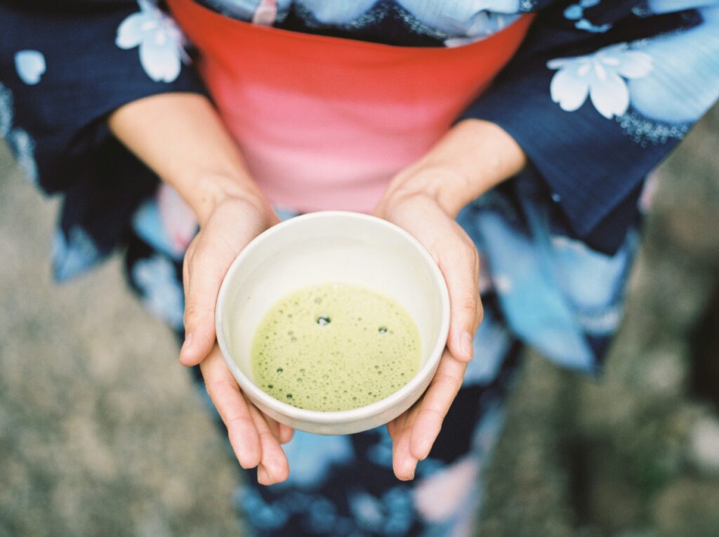 A cup with green tea in hands of kimono wearing woman