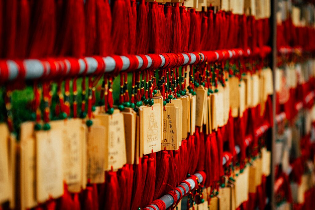 A close-up photograph of traditional wooden prayer plaques, known as ema, hanging in rows with vibrant red tassels at a temple or shrine