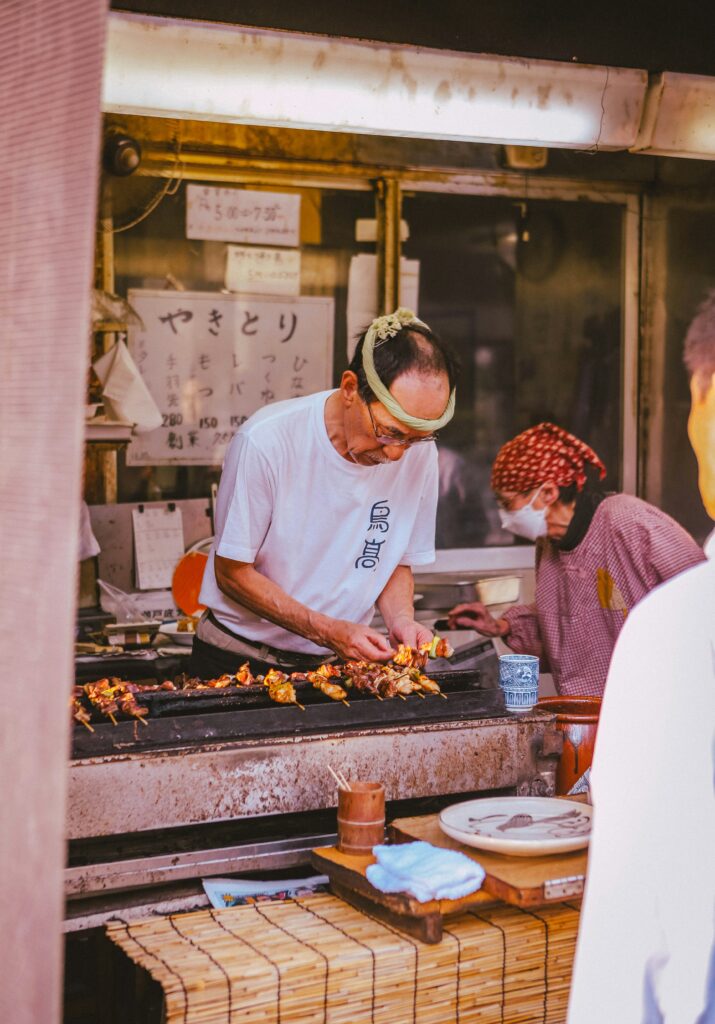 A street food vendor in Japan grilling yakitori skewers at a traditional food stall